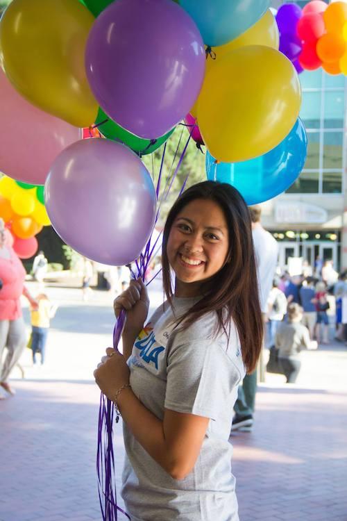 A student in a UCLA LGBT Campus Resource Center t-shirt holds a bunch of colorful balloons while smiling cheerfully.